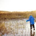 Preschool boy is playing on the ice of a frozen lake or river on a cold sunny winter sunset. Child sliding and having fun with during family hiking. Kids outdoor games in winter