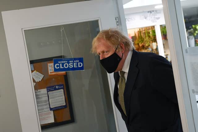 Prime Minister Boris Johnson walks past a sign reading 'We are Closed' during a visit to a Barber shop (Photo by Justin Tallis - WPA Pool/Getty Images)