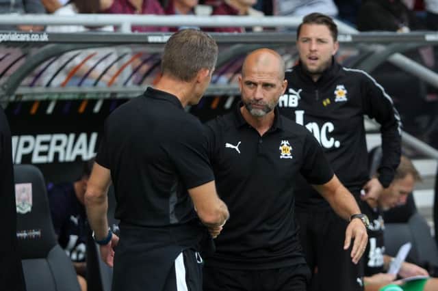 Mark Bonner is pictured in the background as Dean Austin and Joe Dunne, both of whom have since been sacked, shake hands ahead of Cambridge's visit to Cobblers back in August.